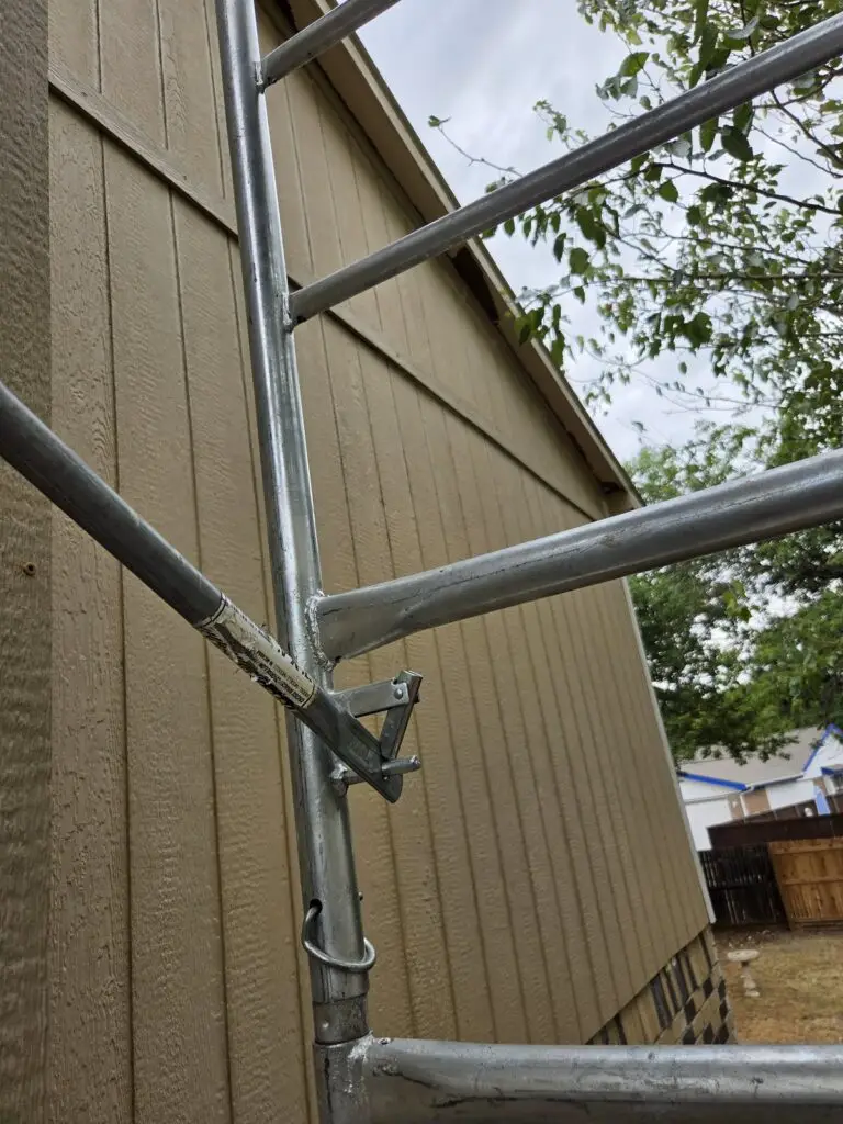 Scaffolding set against a house during an exterior siding replacement, with freshly installed panels running up the wall