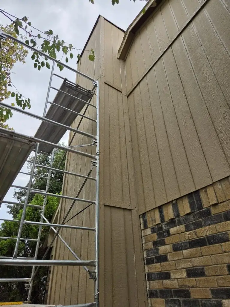 New lap siding installed across a two-story gable end, with scaffolding still in place and the original stone veneer below